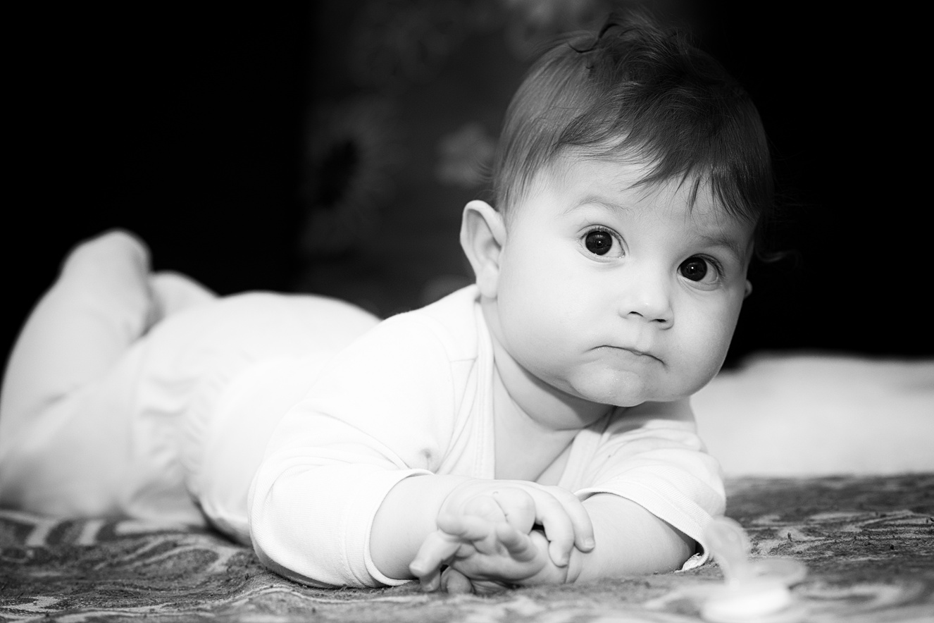 Baby boy is lying on tummy. The baby boy poses and plays with a pacifier. Black white photo